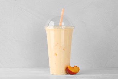 Photo of Plastic cup of tasty smoothie and fresh peach on white wooden table