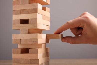 Photo of Playing Jenga. Man removing wooden block from tower at table against grey background, closeup