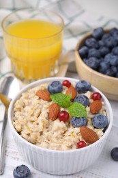 Photo of Oatmeal served with berries. almonds and mint on white table