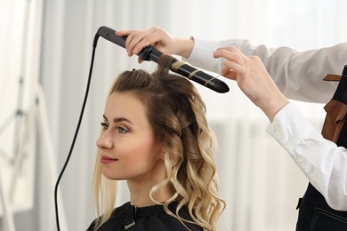 Photo of Hair styling. Hairdresser curling woman's hair in salon, closeup