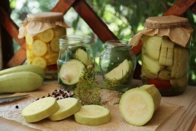 Photo of Cut fresh zucchini and jars of pickled vegetables on white wooden table
