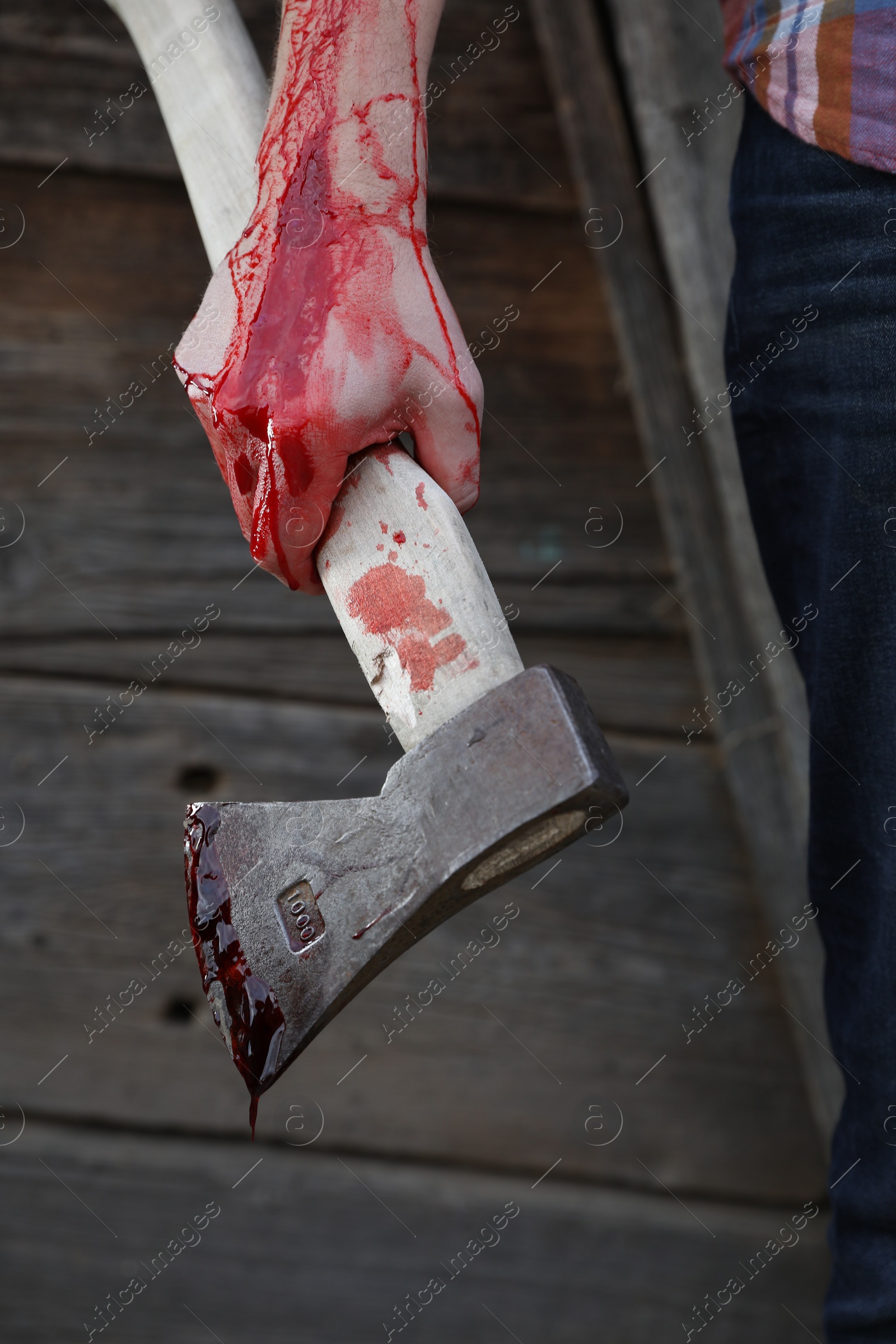 Photo of Man holding bloody axe outdoors, closeup view