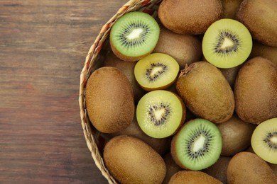 Photo of Basket of many whole and cut fresh kiwis on wooden table, top view