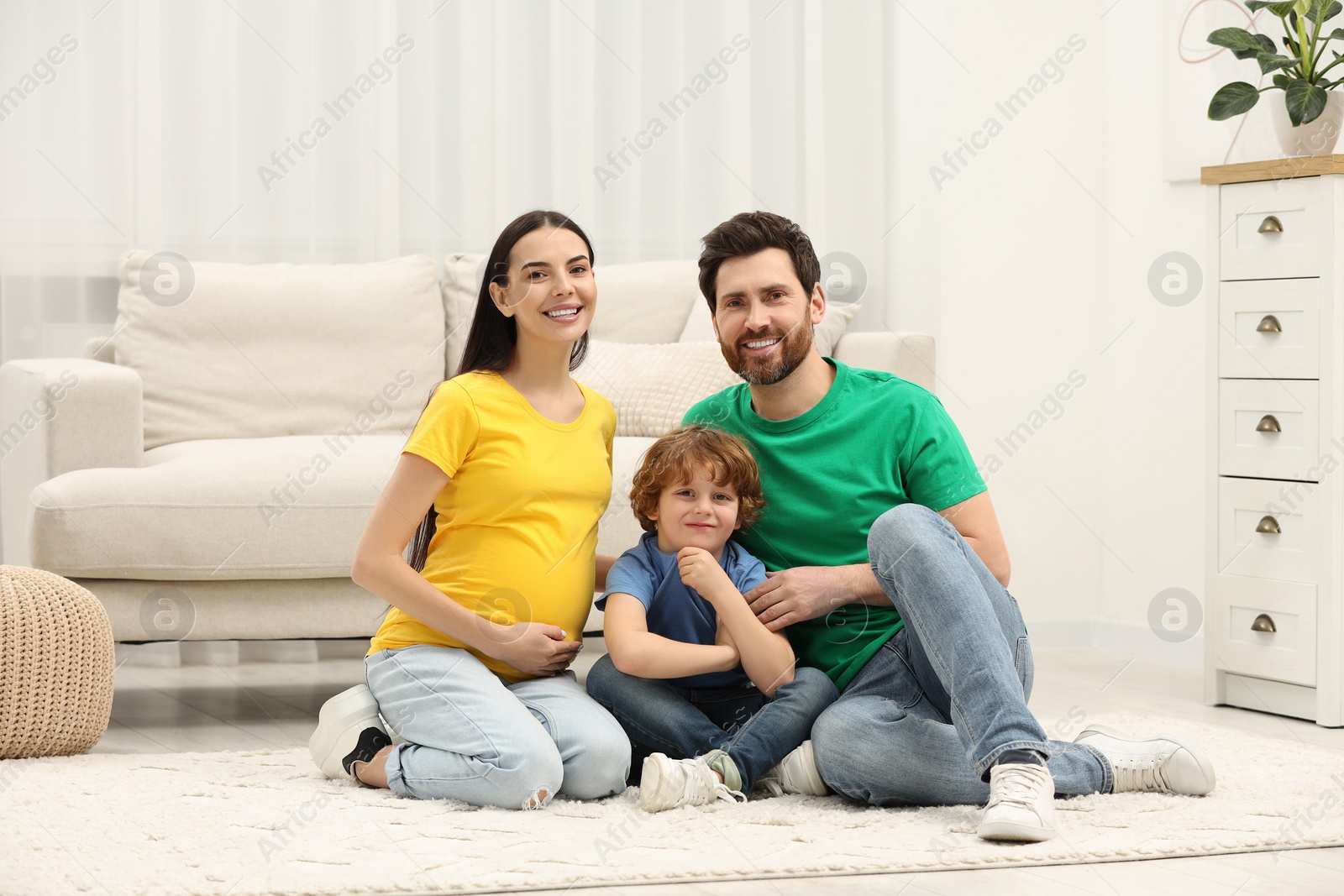 Photo of Family portrait of pregnant mother, father and son sitting on floor in house