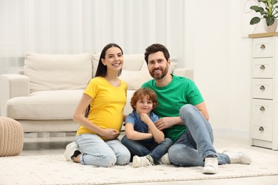 Photo of Family portrait of pregnant mother, father and son sitting on floor in house