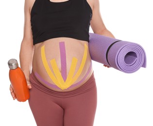 Sporty pregnant woman with kinesio tapes holding water bottle and mat on white background, closeup