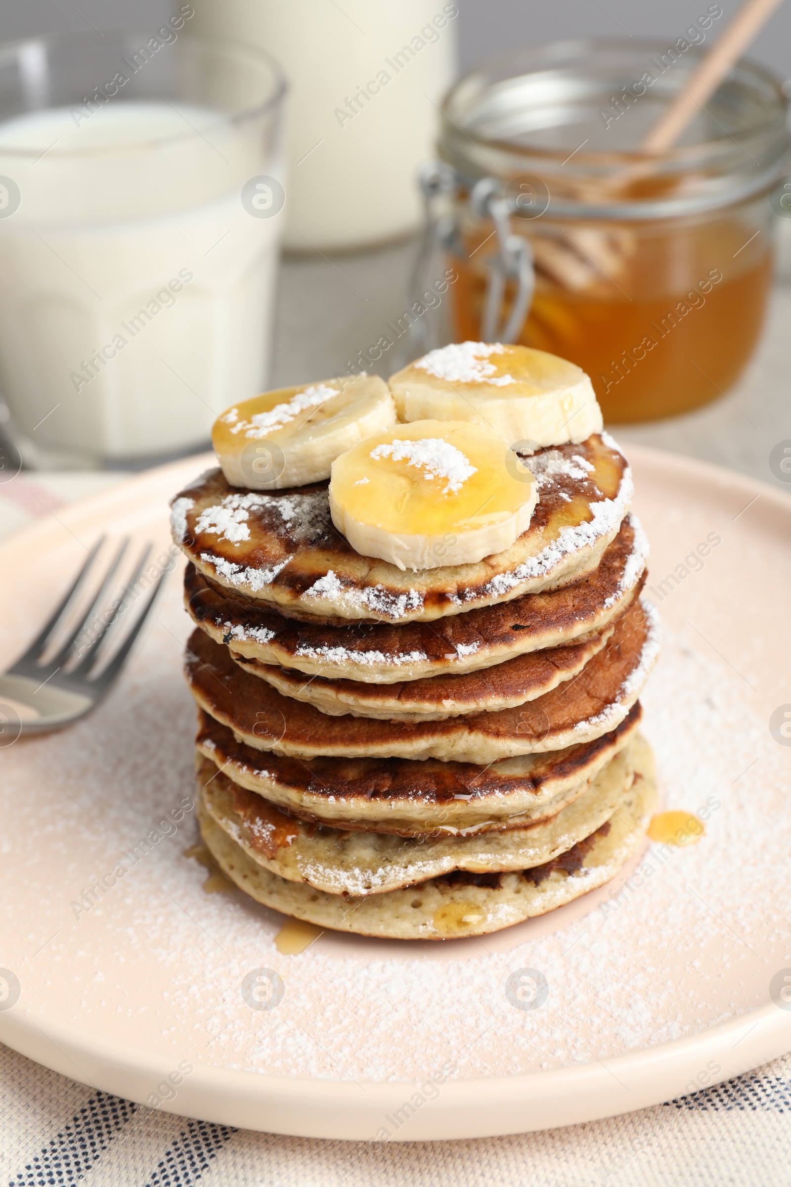 Photo of Plate of banana pancakes with honey and powdered sugar served on table, closeup