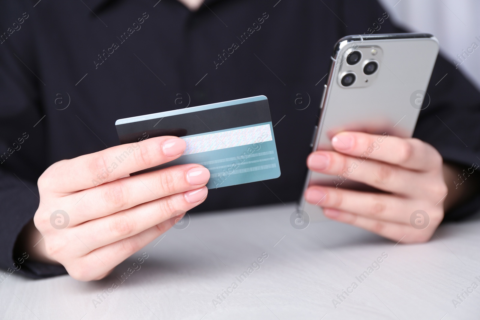 Photo of Online payment. Woman with smartphone and credit card at white wooden table, closeup