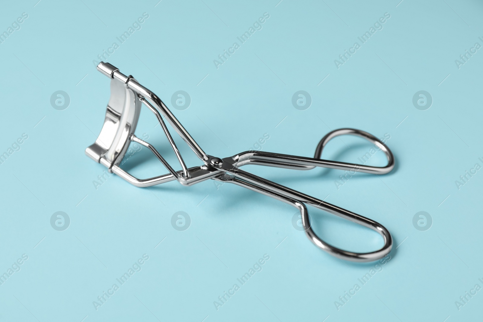 Photo of Eyelash curler on light blue background. Makeup tool