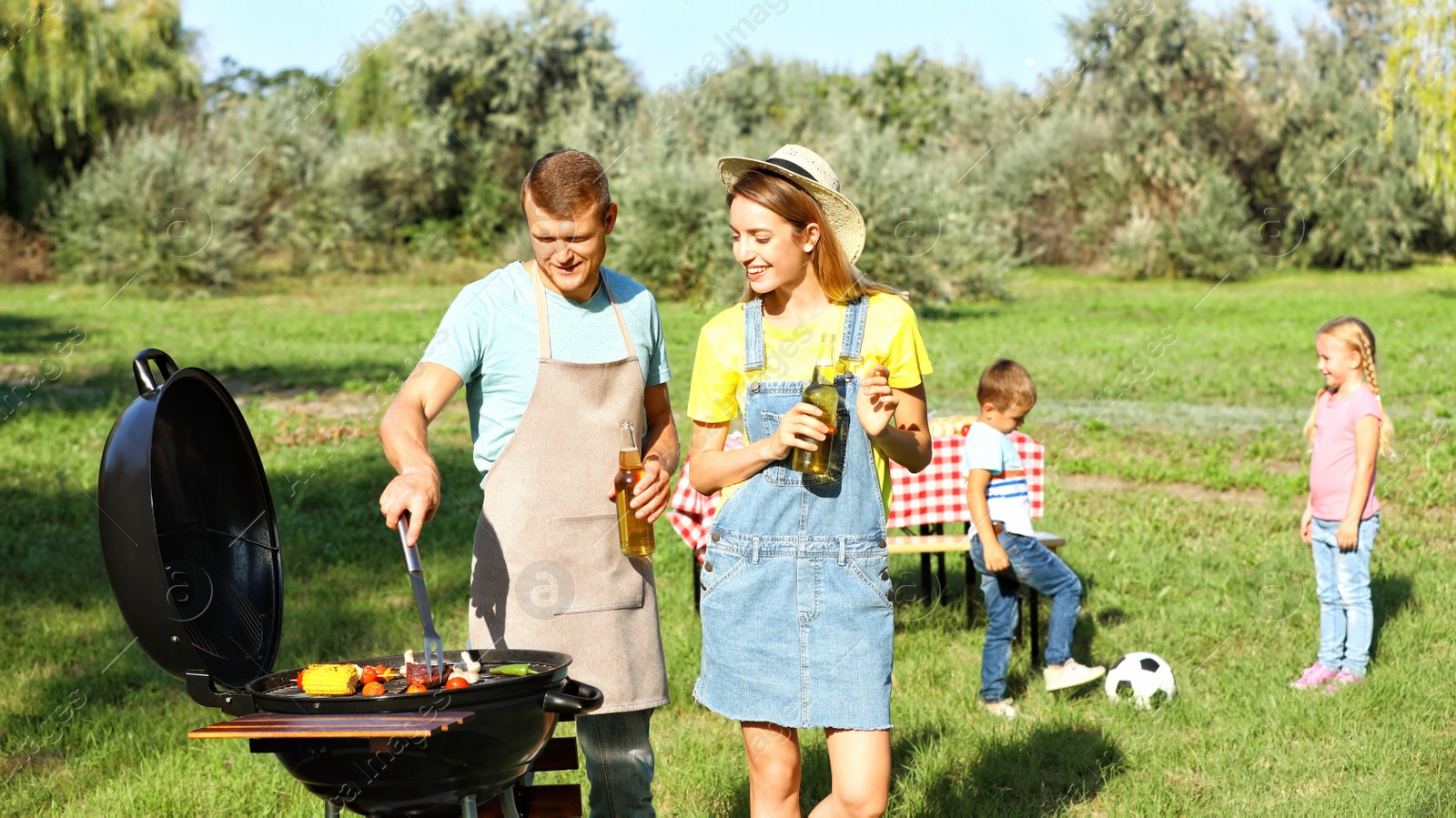 Photo of Happy family with little children having barbecue in park