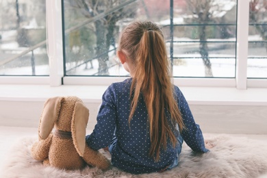 Photo of Lonely little girl with toy sitting near window indoors. Autism concept