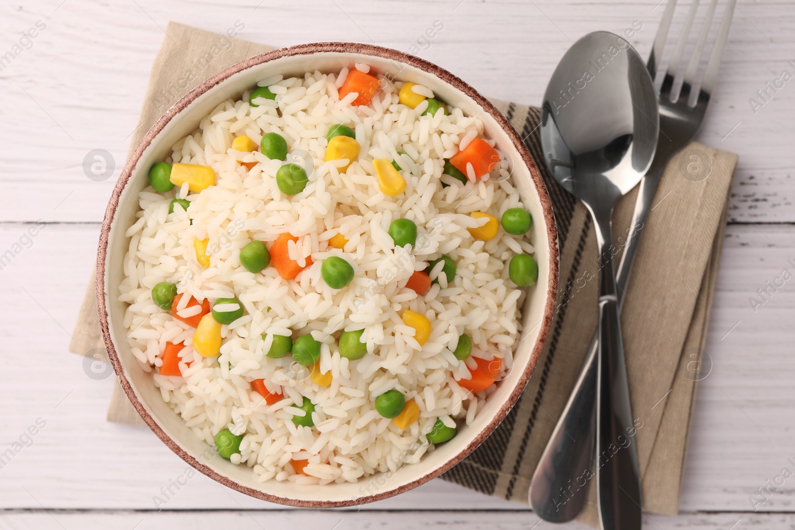 Photo of Bowl of delicious rice with vegetables served on white wooden table, flat lay