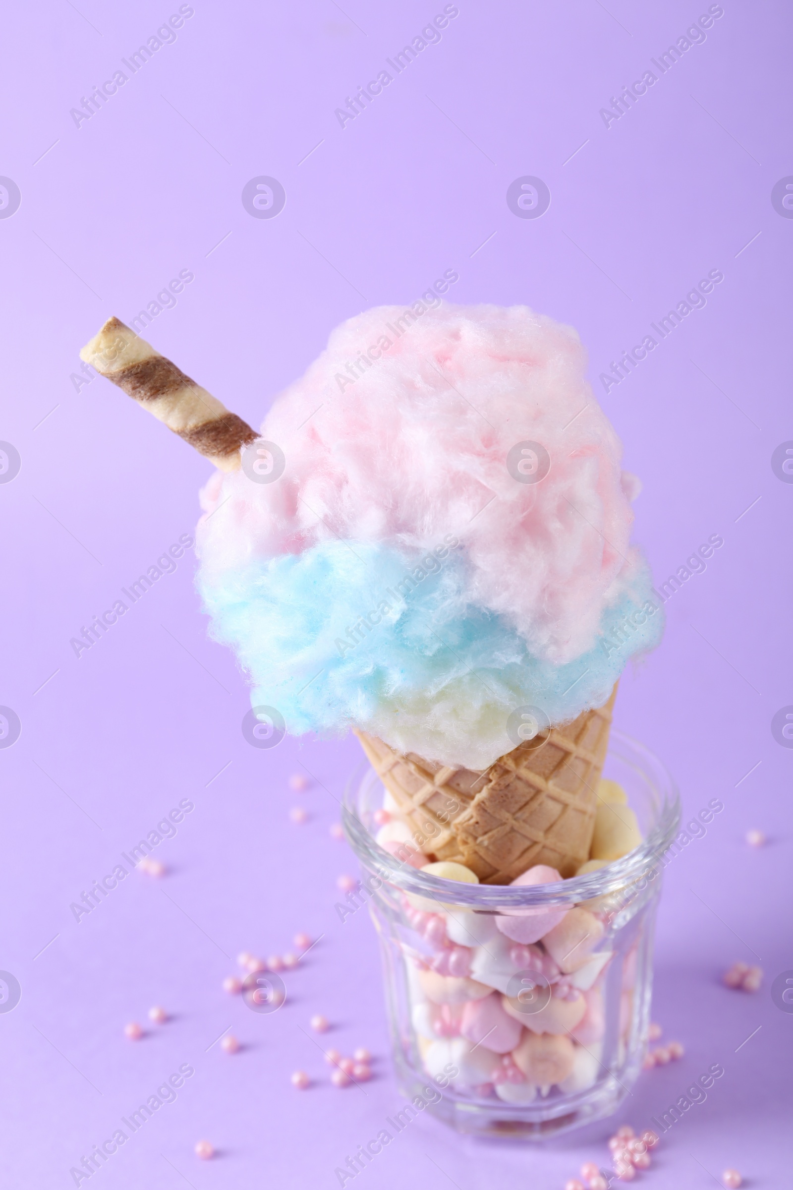 Photo of Sweet cotton candy in waffle cone on purple background, closeup