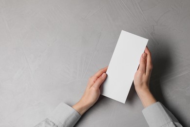 Woman holding blank card at light grey table, top view. Mockup for design