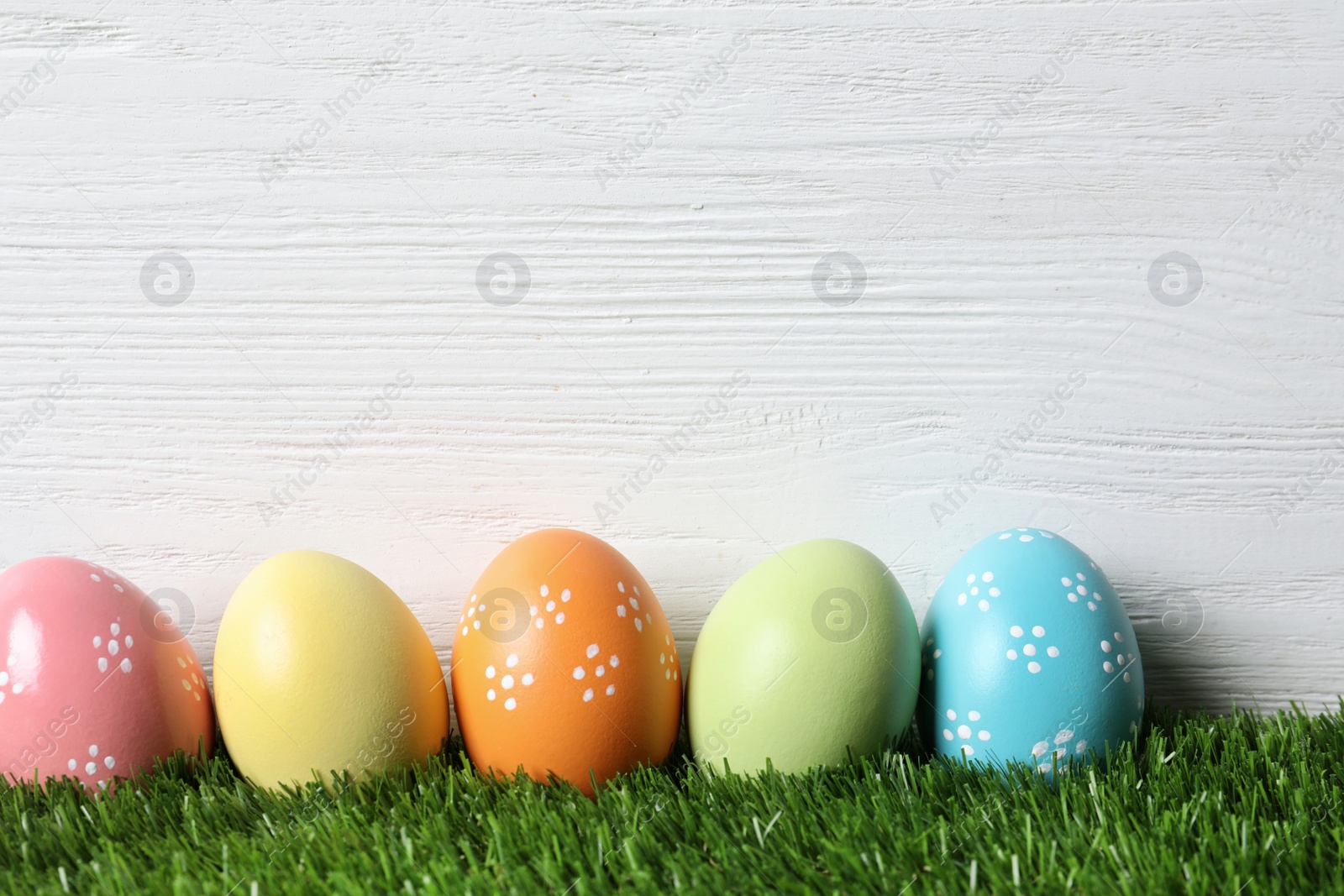 Photo of Colorful painted Easter eggs on green grass against wooden background, space for text