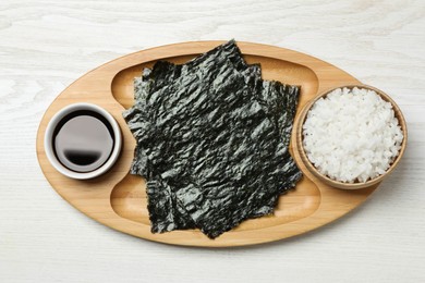Photo of Tray with dry nori sheets, rice and soy sauce on white wooden table, top view