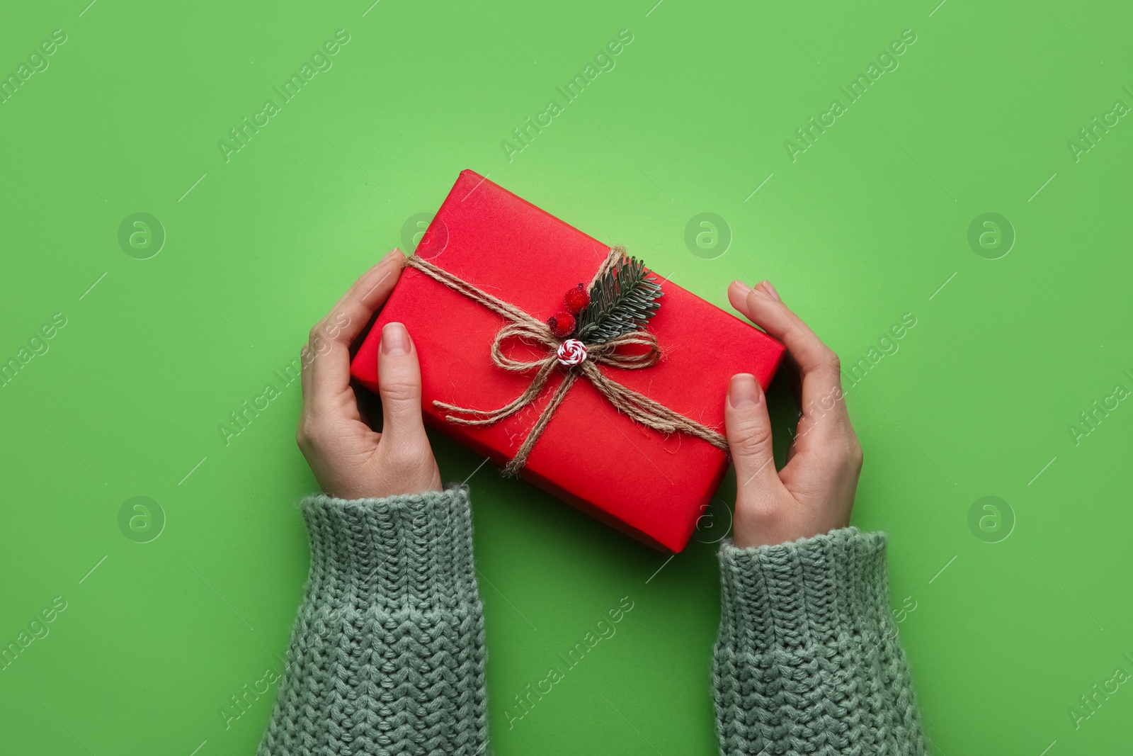 Photo of Woman holding Christmas gift box on green background, top view