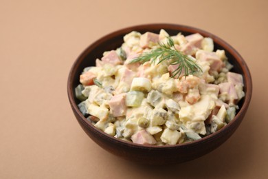 Tasty Olivier salad with boiled sausage in bowl on beige table