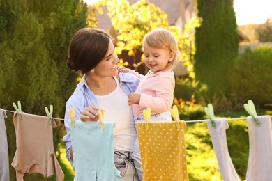 Photo of Mother and daughter hanging clothes with clothespins on washing line for drying in backyard