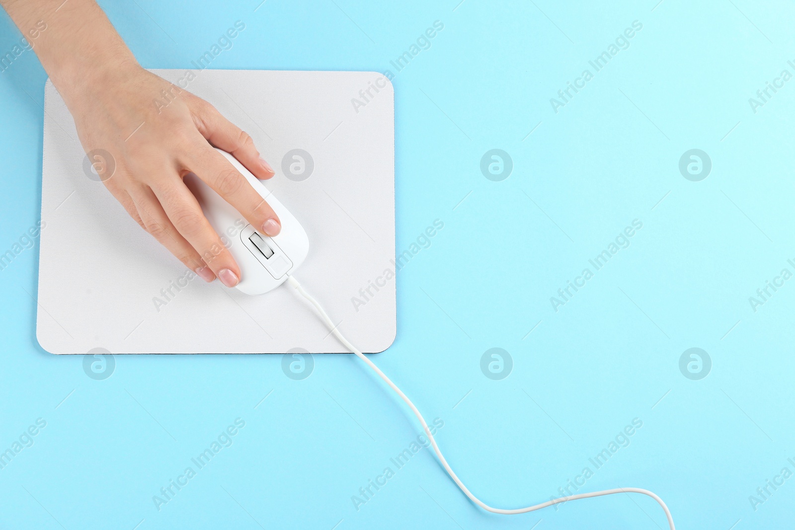 Photo of Woman with modern wired optical mouse and pad on light blue background, top view. Space for text