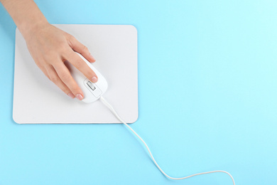 Woman with modern wired optical mouse and pad on light blue background, top view. Space for text