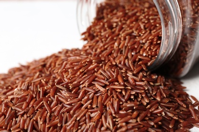 Pile of brown rice and jar on white background, closeup