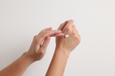 Woman applying cosmetic cream onto hand on white background, closeup