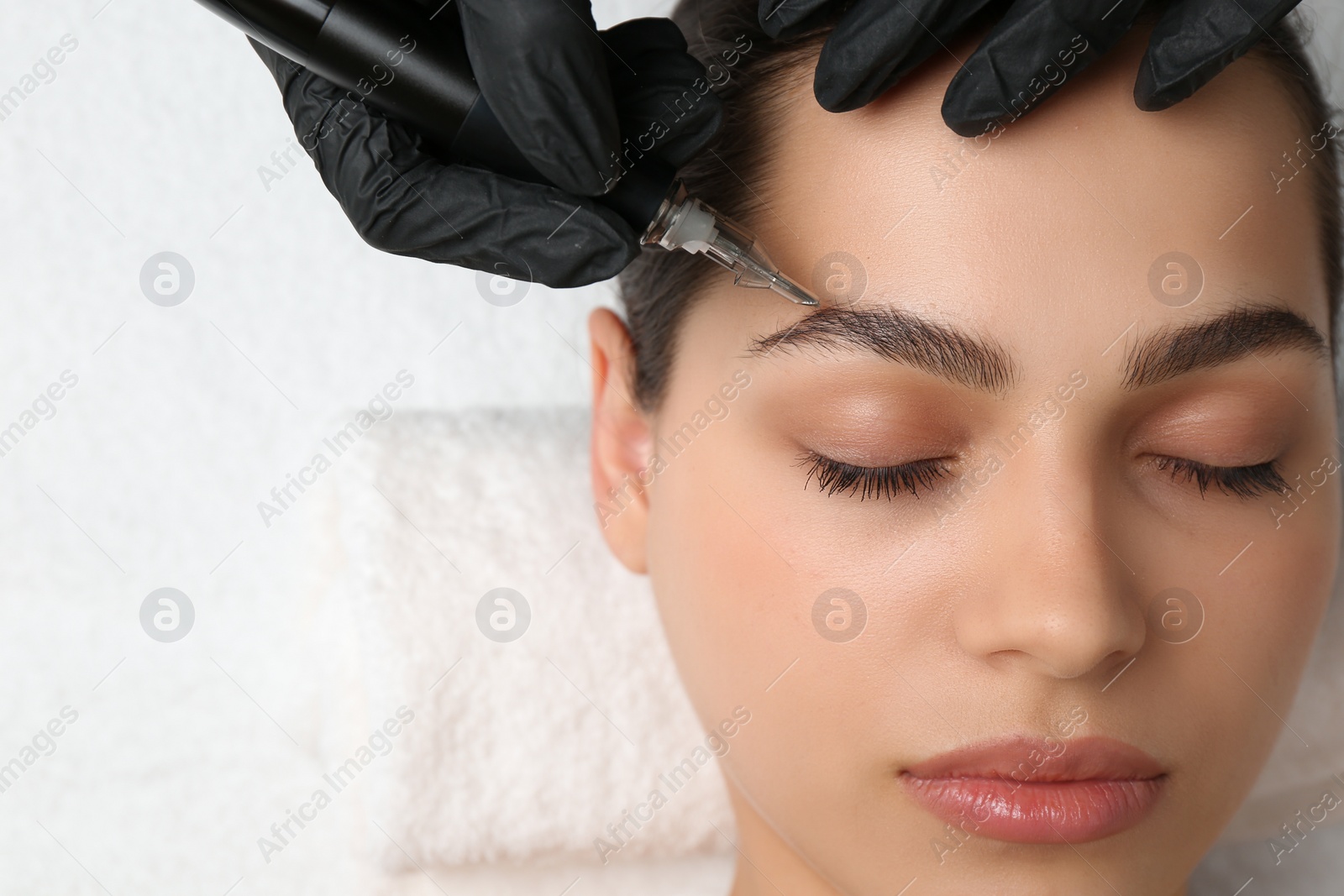 Photo of Beautician making permanent eyebrow makeup to young woman, top view. Space for text