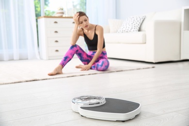 Photo of Scales on floor and sad young woman at home. Weight loss motivation