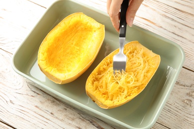 Woman scraping flesh of cooked spaghetti squash with fork on table