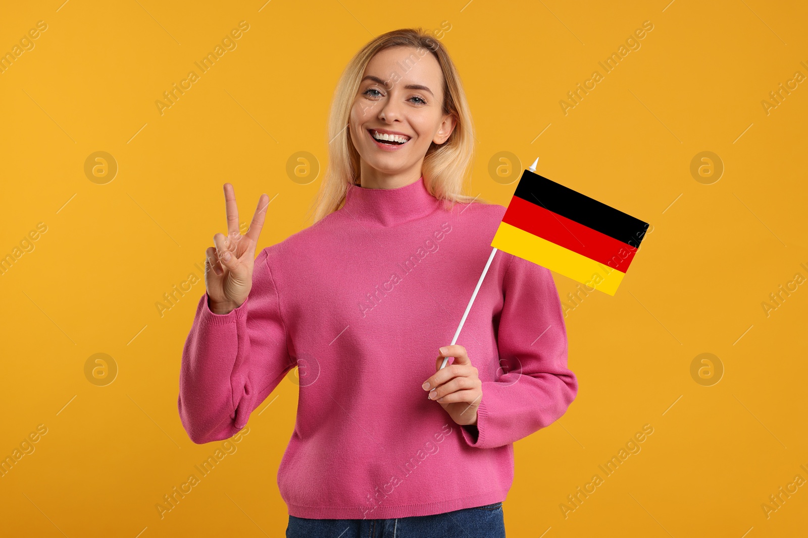 Image of Happy young woman with flag of Germany showing V-sign on yellow background