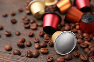 Many coffee capsules and beans on wooden table, closeup