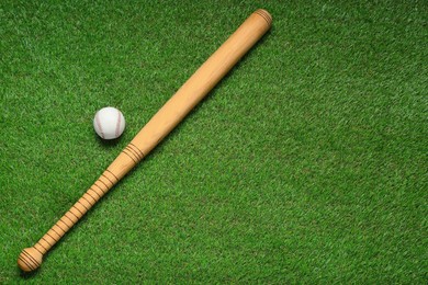 Photo of Wooden baseball bat and ball on green grass, flat lay. Space for text