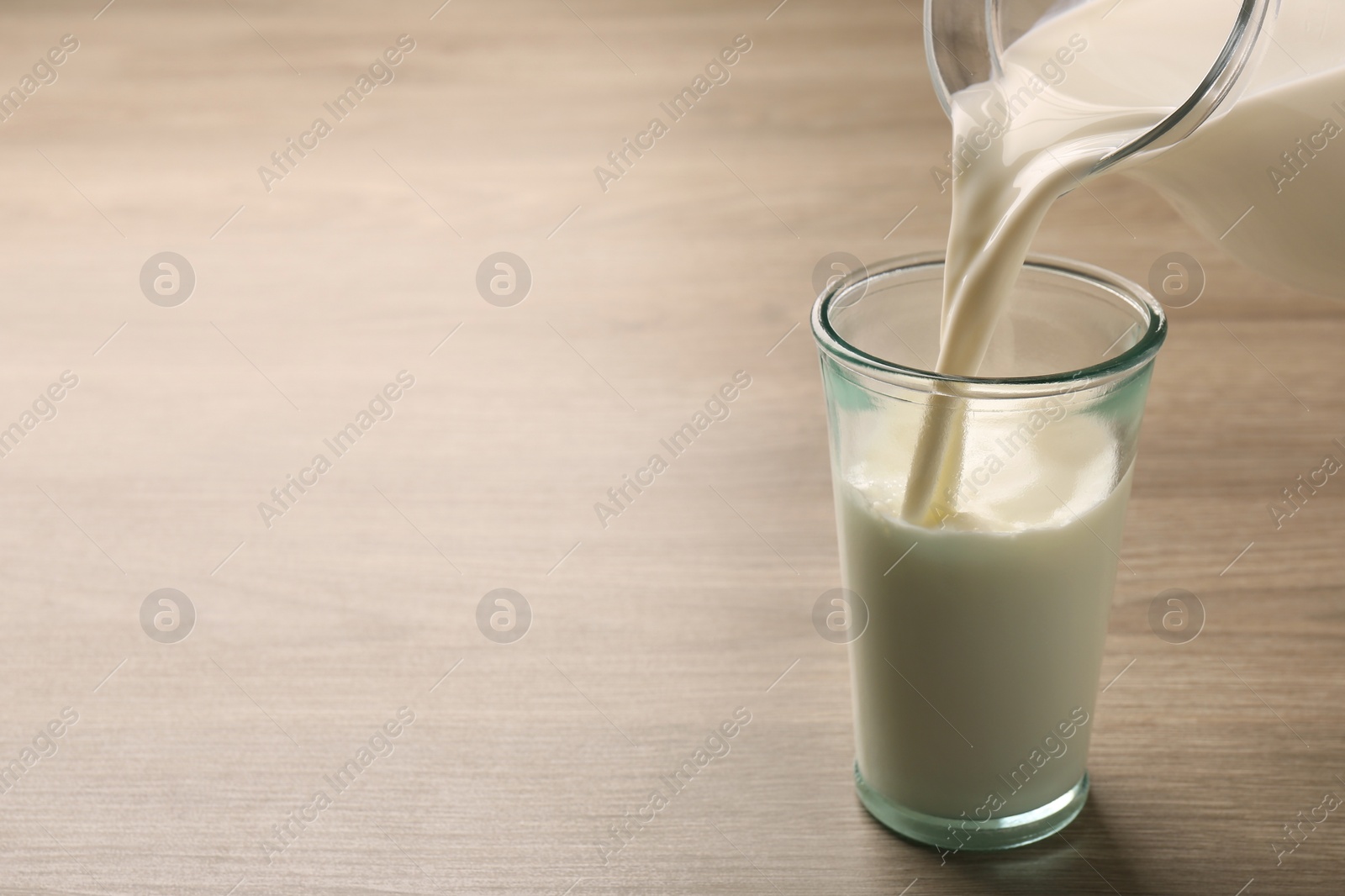 Photo of Pouring tasty milk into glass on wooden table, closeup. Space for text
