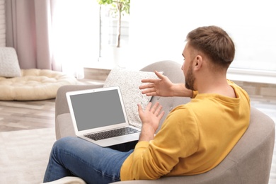 Photo of Young man using video chat on laptop in living room. Space for design