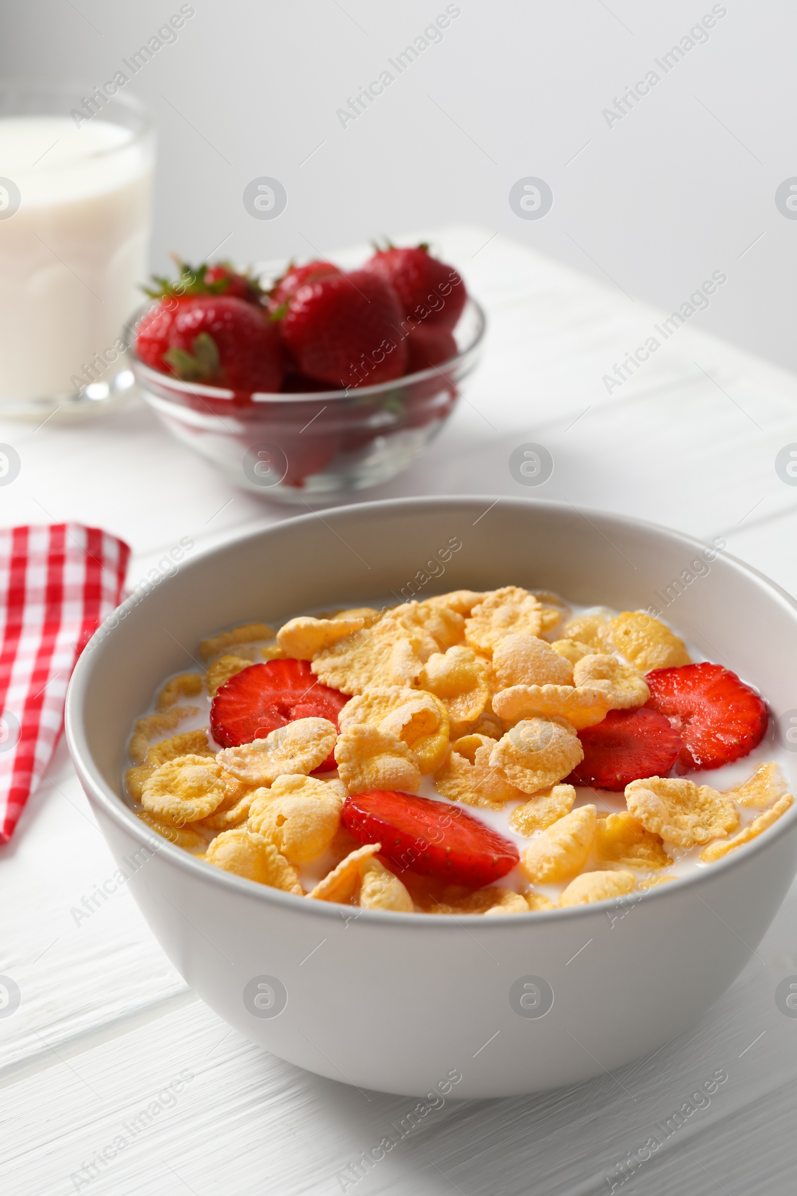 Photo of Corn flakes with strawberries in bowl served on white wooden table