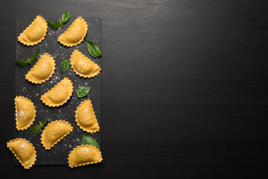 Raw ravioli with basil on black table, flat lay and space for text. Italian pasta