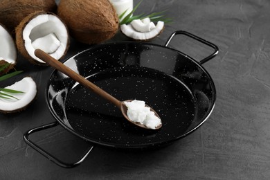 Photo of Frying pan with organic coconut cooking oil, wooden spoon and fresh fruits on grey table