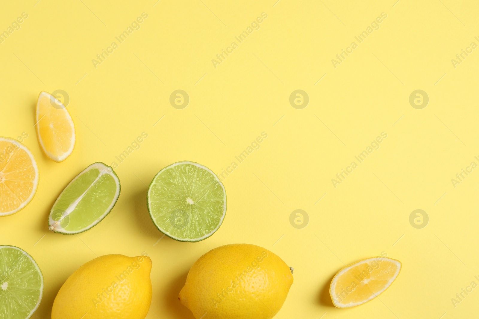 Photo of Fresh ripe lemons and limes on yellow background, flat lay. Space for text