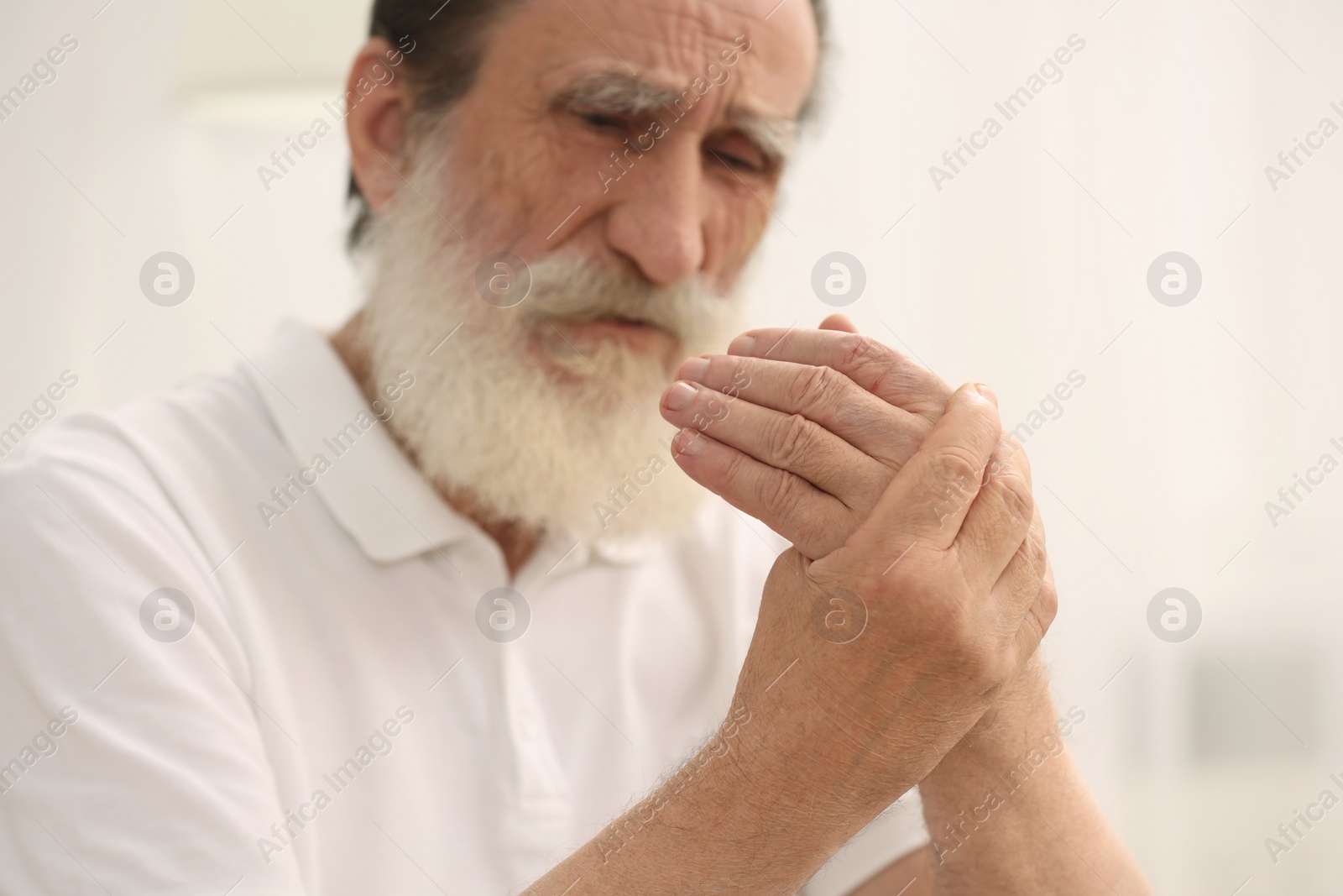 Photo of Senior man suffering from pain in hand indoors, selective focus. Rheumatism symptom