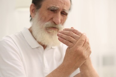 Senior man suffering from pain in hand indoors, selective focus. Rheumatism symptom