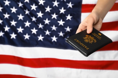 Woman holding passport against flag of USA, closeup with space for text