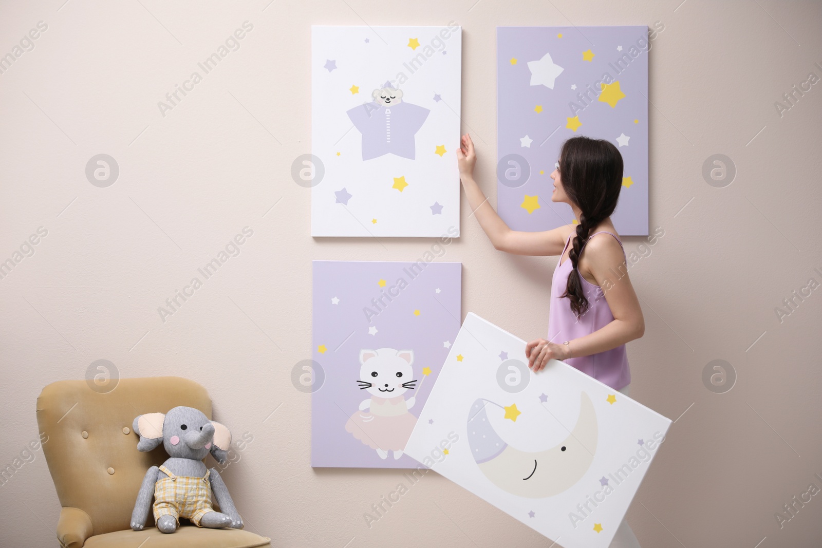 Photo of Decorator hanging pictures on pink wall. Children's room interior design