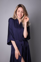 Photo of Pretty young woman in beautiful dark blue silk robe on grey background