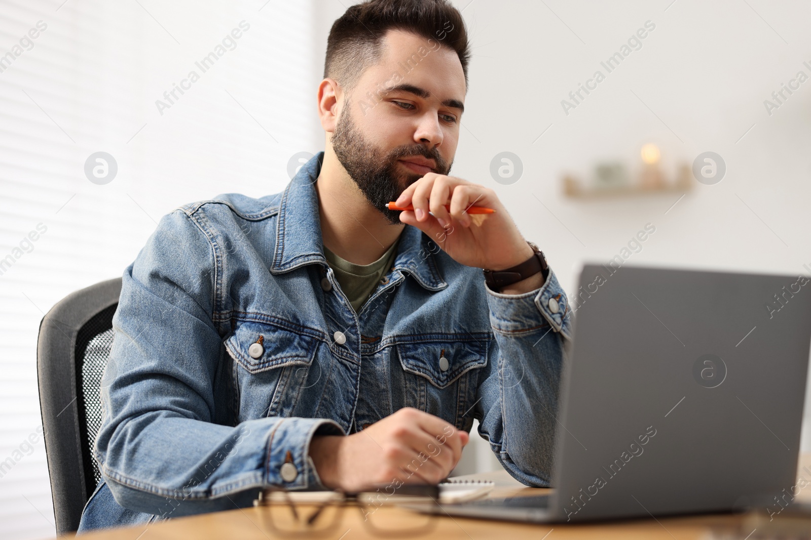 Photo of Young man watching webinar at table in room