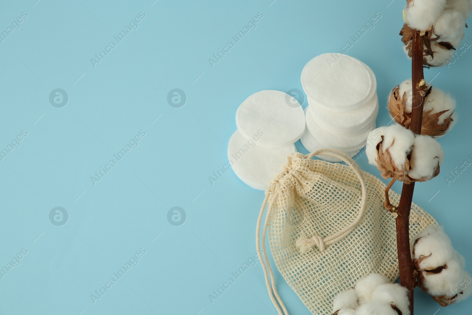 Photo of Bag, cotton pads and flowers on light blue background. Space for text