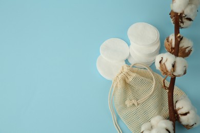 Photo of Bag, cotton pads and flowers on light blue background. Space for text