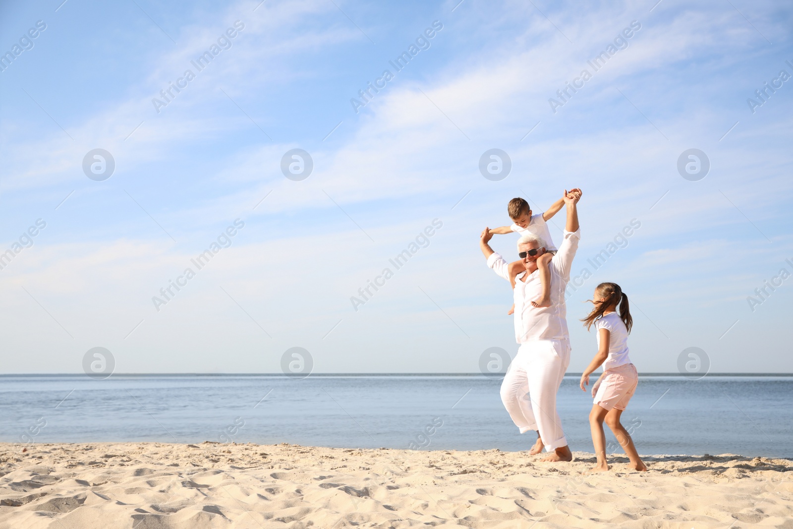 Photo of Cute little children with grandfather spending time together on sea beach