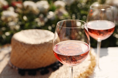 Glasses of rose wine on white table in blooming garden, closeup. Space for text