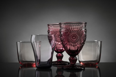 Photo of Set of different colorful empty glasses on table against grey background